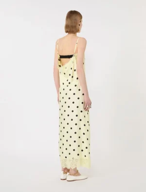 Back view of a woman wearing a pale yellow spaghetti-strap polka-dot slip dress with lace trim at the hem.