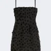 Black mini dress with polka dot texture and thin spaghetti straps, fitted bodice and pockets at the hips