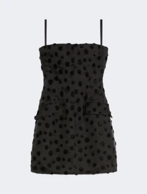 Black mini dress with polka dot texture and thin spaghetti straps, fitted bodice and pockets at the hips