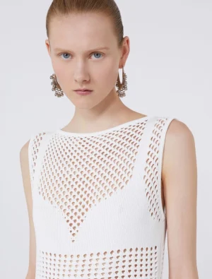 Model wearing a white sleeveless knit top with mesh panels and large metallic hoop earrings, facing forward.