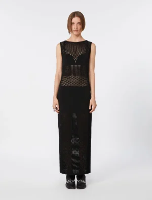 Full-length black mesh maxi dress with perforated panels worn by a female model, paired with black loafers and a simple updo.