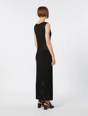 Back view of a woman wearing a sleeveless black mesh-knit maxi dress with sheer panels and black block-heeled sandals.