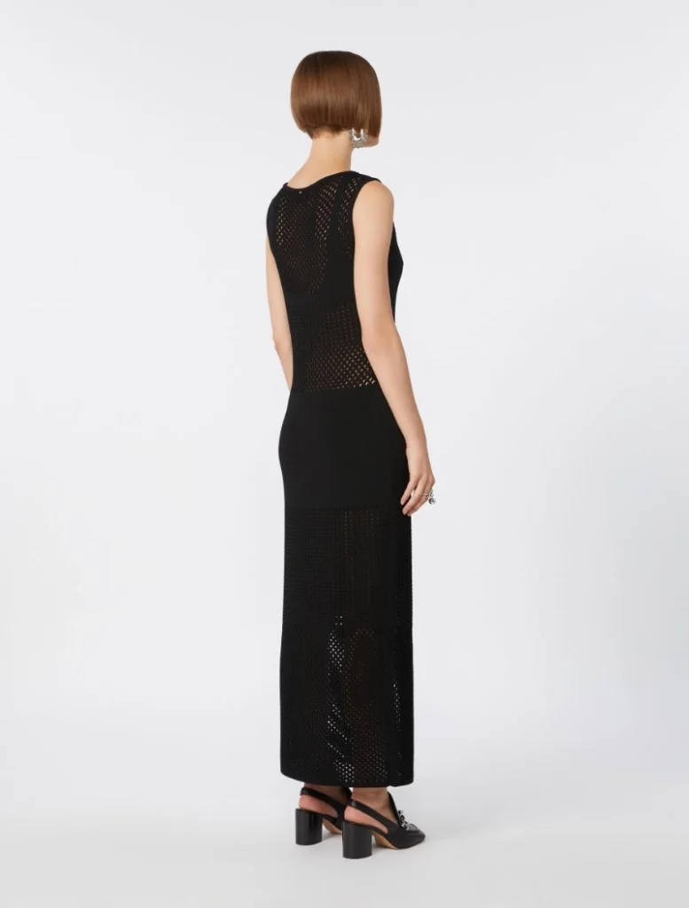 Back view of a woman wearing a sleeveless black mesh-knit maxi dress with sheer panels and black block-heeled sandals.