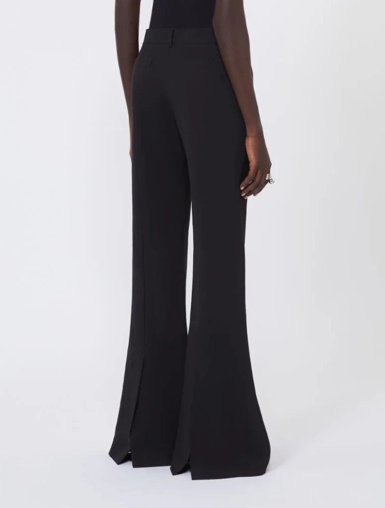 Back view of a model wearing black high-waisted wide-leg trousers with long flared hems.