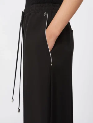 Side view of black wide-leg pants with an elastic drawstring waist, white piping along the side seam, and a hand in the pocket.