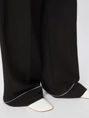 Close-up of black wide-leg pants with white piping at the hem, paired with white pointed-toe shoes.