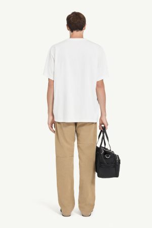 Person standing with back to camera, wearing a white oversized T-shirt, tan cargo pants, and carrying a black bag by the side.