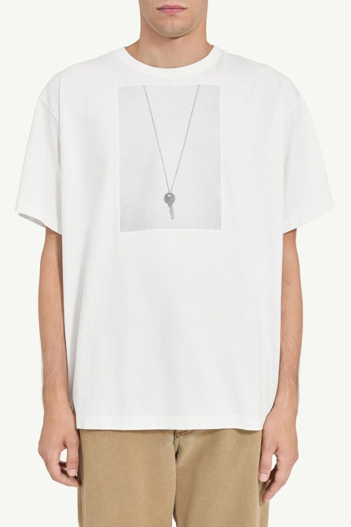 White T-shirt with a grey rectangular graphic showing a delicate silver key pendant on a chain.