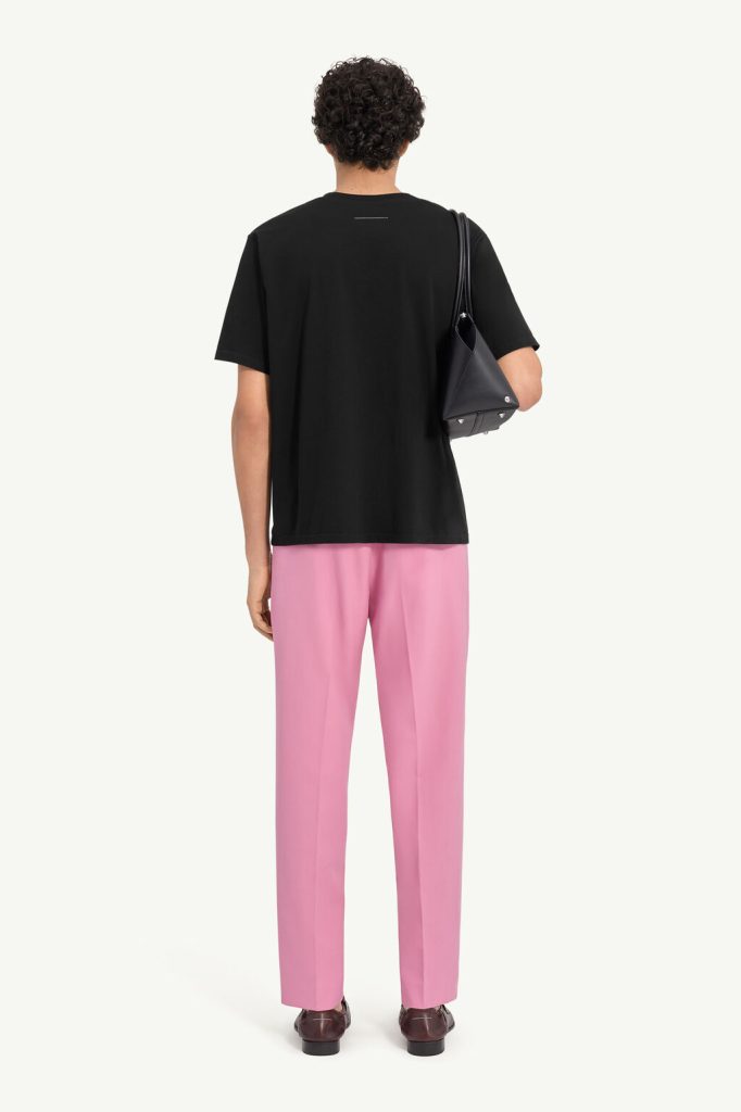 Back view of a person wearing a black T-shirt and pink trousers, carrying a black handbag over the shoulder.