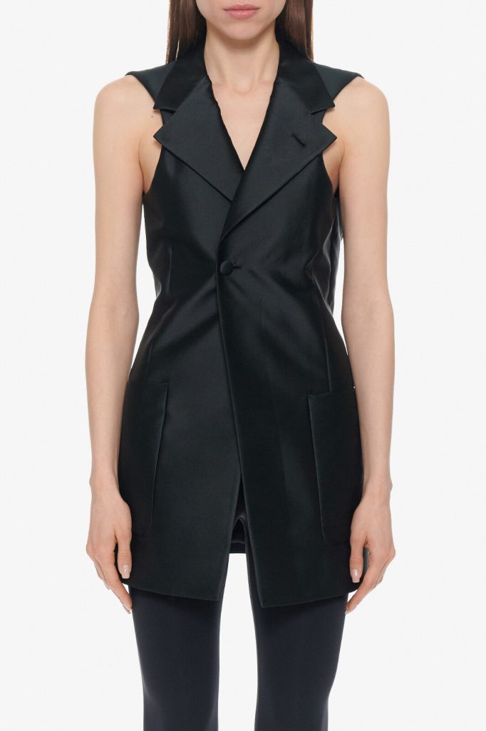 Black sleeveless tailored vest with wide overlapping lapels, single button closure, and front pockets on a model.