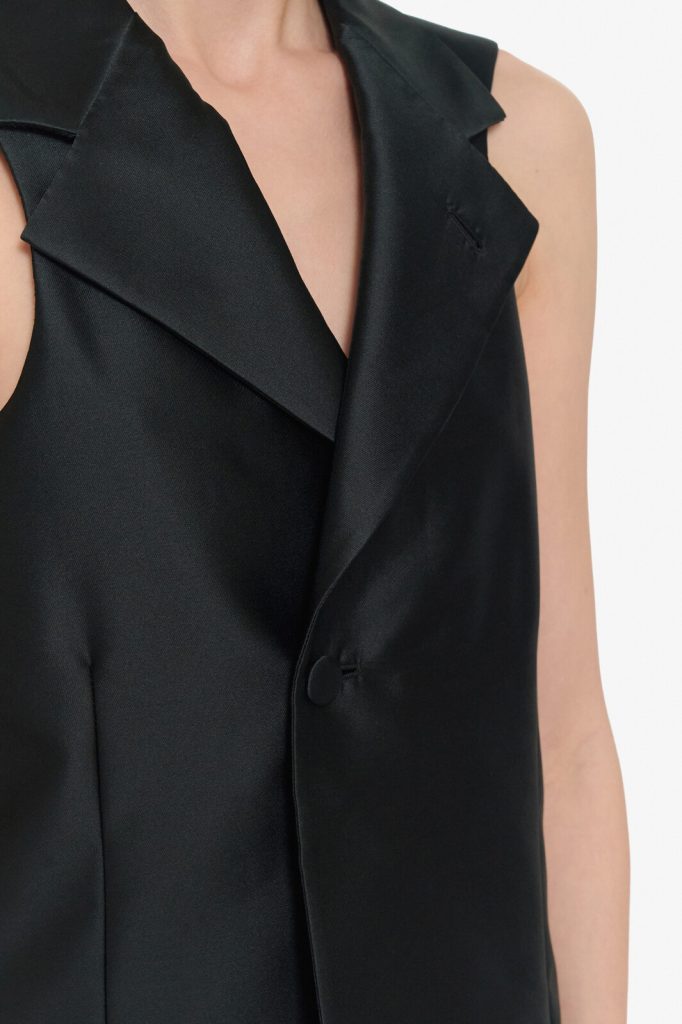 Close-up of a black sleeveless blazer with wide lapels and a single front button on a person
