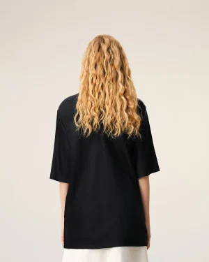 Person with long, curly blonde hair seen from behind, wearing a black top against a pale background