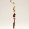 Gold keychain with a circular ring, brown leather cord, and amber beads hanging against a light background.