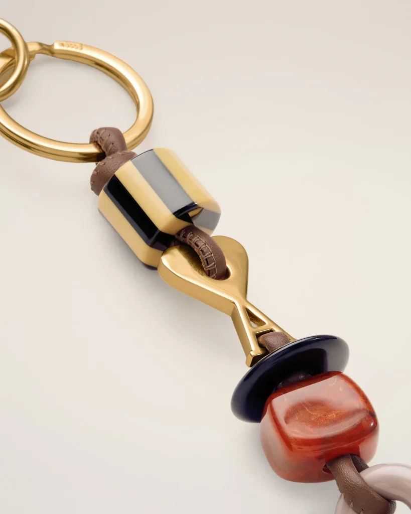 Close-up of a gold-tone bracelet with a brown leather strand and a striped bead (black, beige, gray).