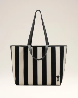 Striped beige and black tote bag with long black handles and a small heart patch near the bottom corner.