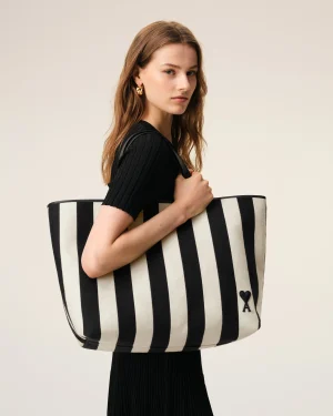 Woman in a black top holding a large black-and-white striped tote bag against a neutral background.