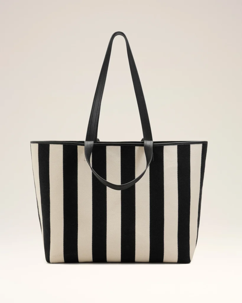 Large striped tote bag with black handles, beige and black vertical stripes against a pale background.