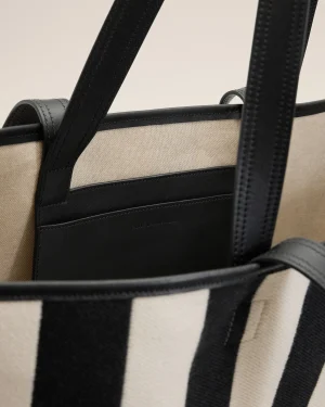 Close-up of a beige canvas bag with black leather trim and thick black straps.