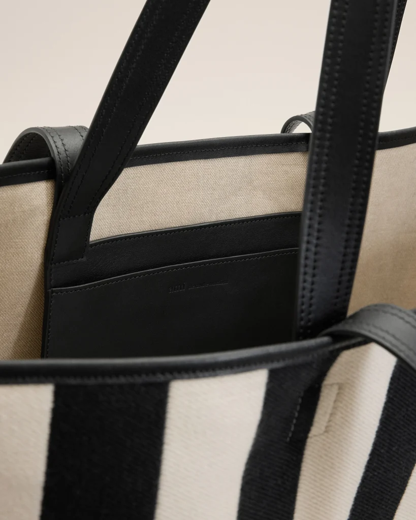 Close-up of a beige canvas bag with black leather trim and thick black straps.