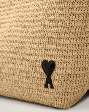 Close-up of a woven straw bag featuring a black leather heart charm hanging from a knot.