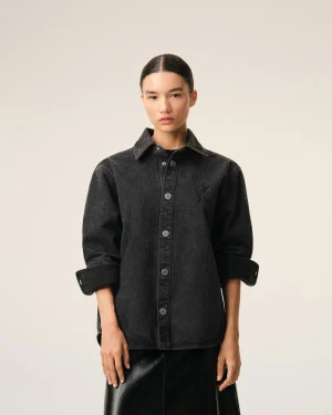 Person wearing a dark denim shirt, facing the camera, against a light beige background (torso shot).