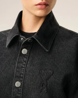 Close-up of a person wearing a dark denim jacket, showing the raised collar, metal buttons, and visible lips at the top of the frame.