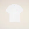 White T-shirt with a small red heart emblem on the left chest against a pale beige background, minimalist style