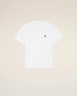 White T-shirt with a small red heart emblem on the left chest against a pale beige background, minimalist style