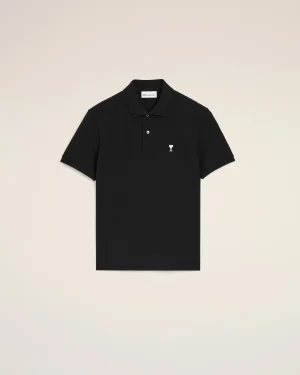 Black polo shirt with a small white heart emblem on the left chest against a beige background.
