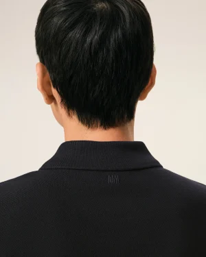 Back of a person’s head with short black hair, wearing a dark polo shirt; neutral beige background.