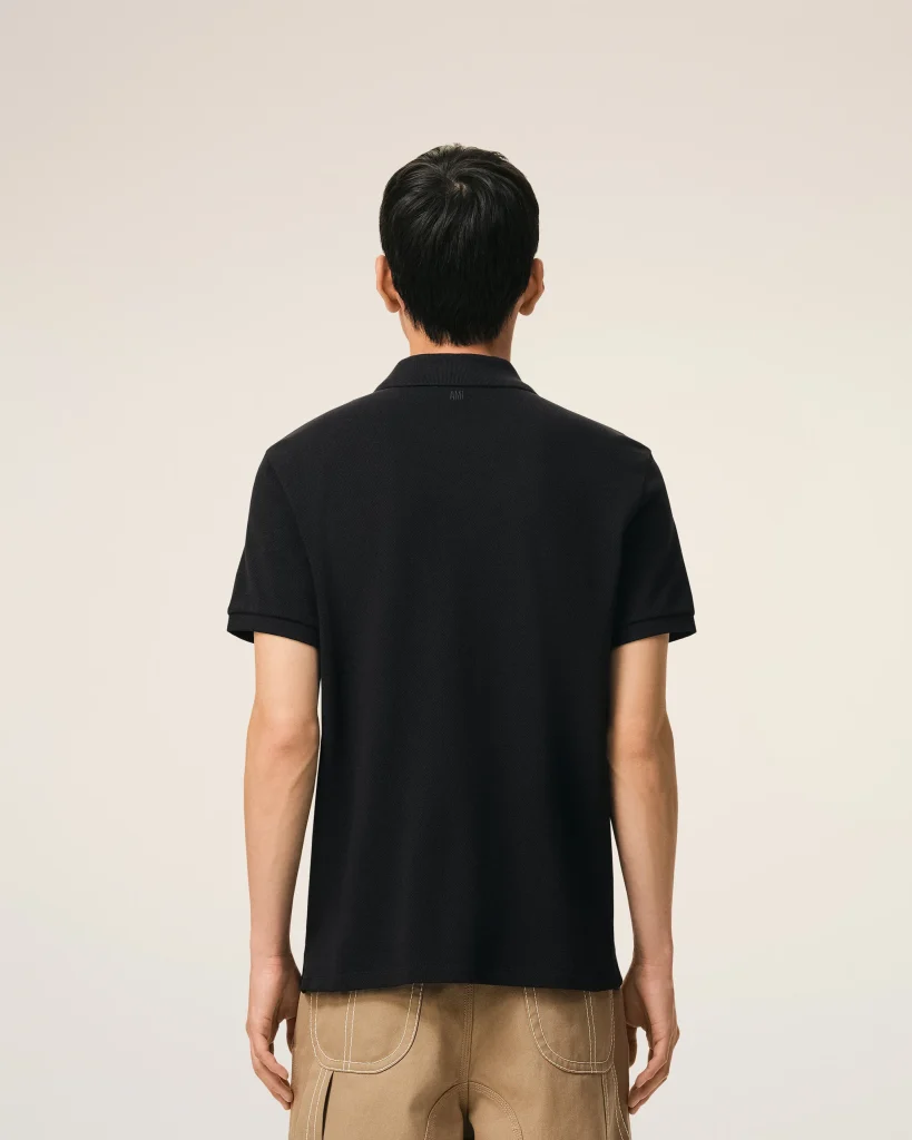 Back view of a person wearing a black polo shirt and tan pants, showing the shirt’s collar and back pockets stitching unmistakable in view beneath a plain background.