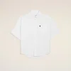 White short-sleeve button-down shirt laid flat on a beige background, with a small black heart on the left chest pocket.