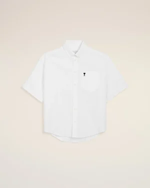 White short-sleeve button-down shirt laid flat on a beige background, with a small black heart on the left chest pocket.