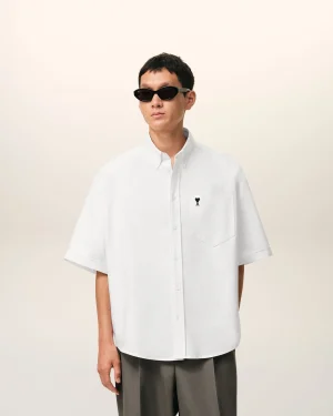Person wearing a loose white button-down shirt and dark sunglasses against a pale backdrop, posing sideways. (Informative fashion image)