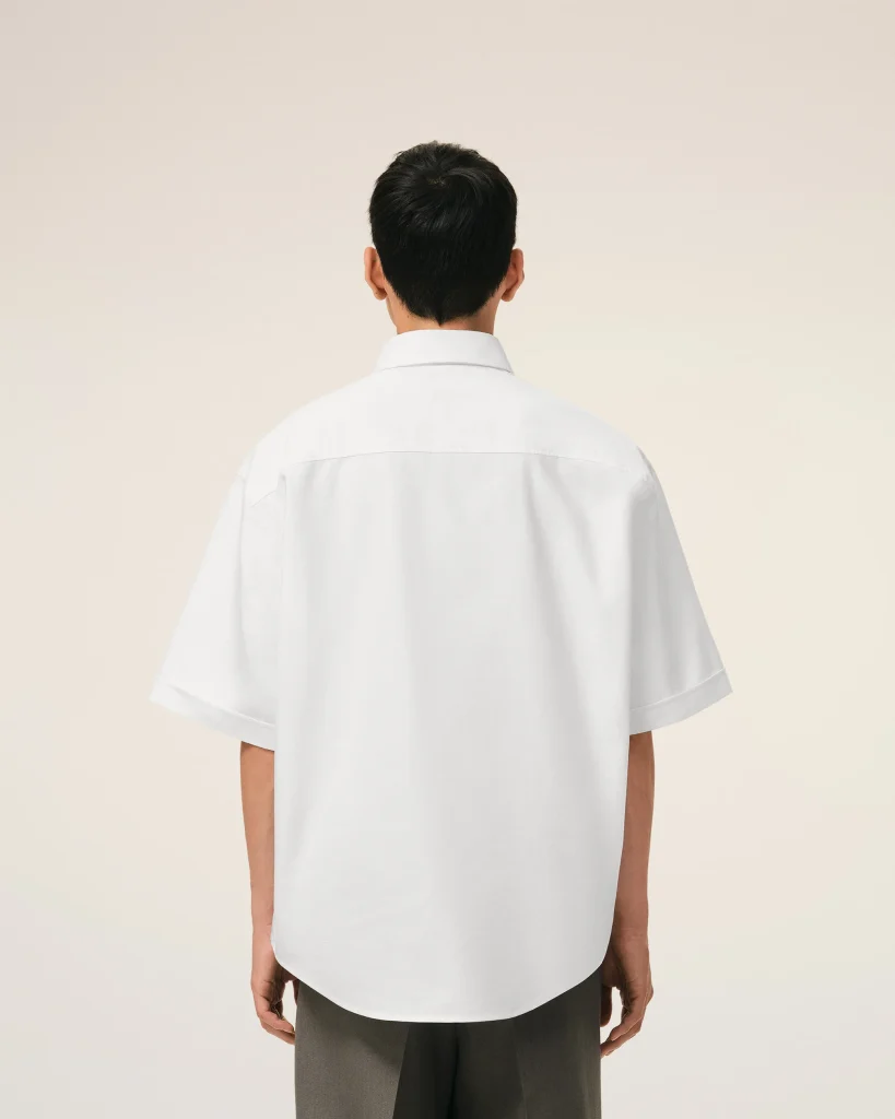 Back view of a person wearing a white shirt standing against a beige wall