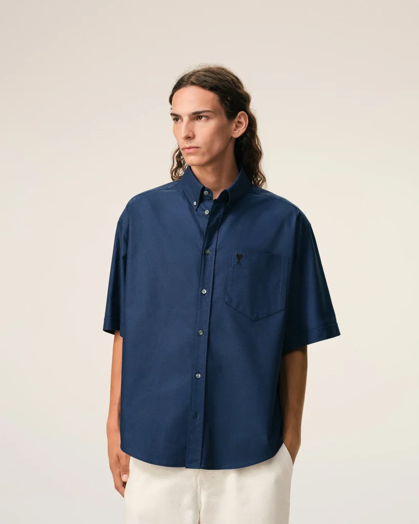 Person wearing a navy blue button-down shirt with a chest pocket, standing against a pale background.