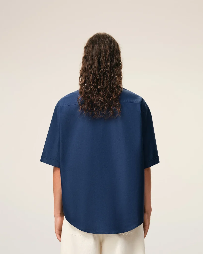 Person facing away from the camera with long curly hair and a blue shirt, neutral light background.