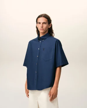 Person wearing a navy blue short-sleeve button-down shirt, facing the camera against a light beige backdrop.