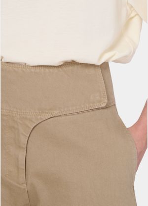 Close-up of beige high-waisted pants with a wide waistband and curved front pocket, tucked white top showing.