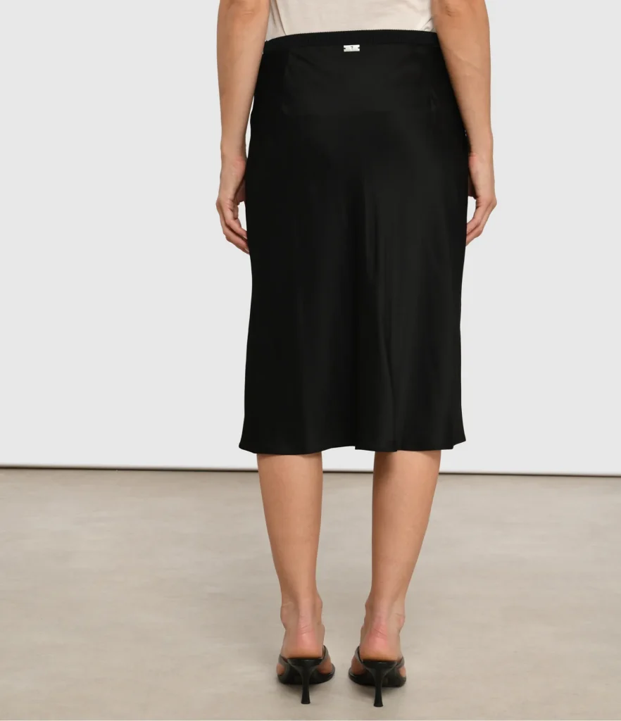 Back view of a person wearing a black midi skirt, beige top, and black heeled sandals.