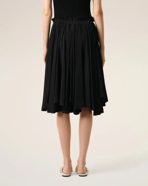 Back view of a person wearing a black dress with a ruched waistband and flat sandals.