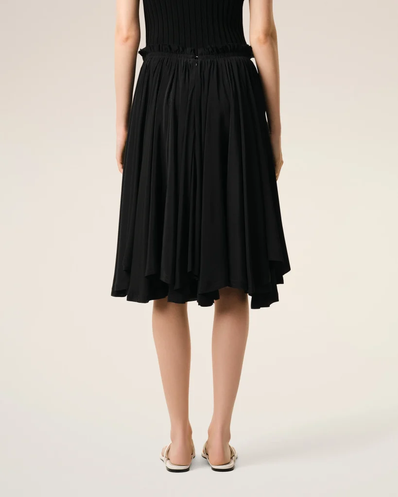 Back view of a person wearing a black dress with a ruched waistband and flat sandals.