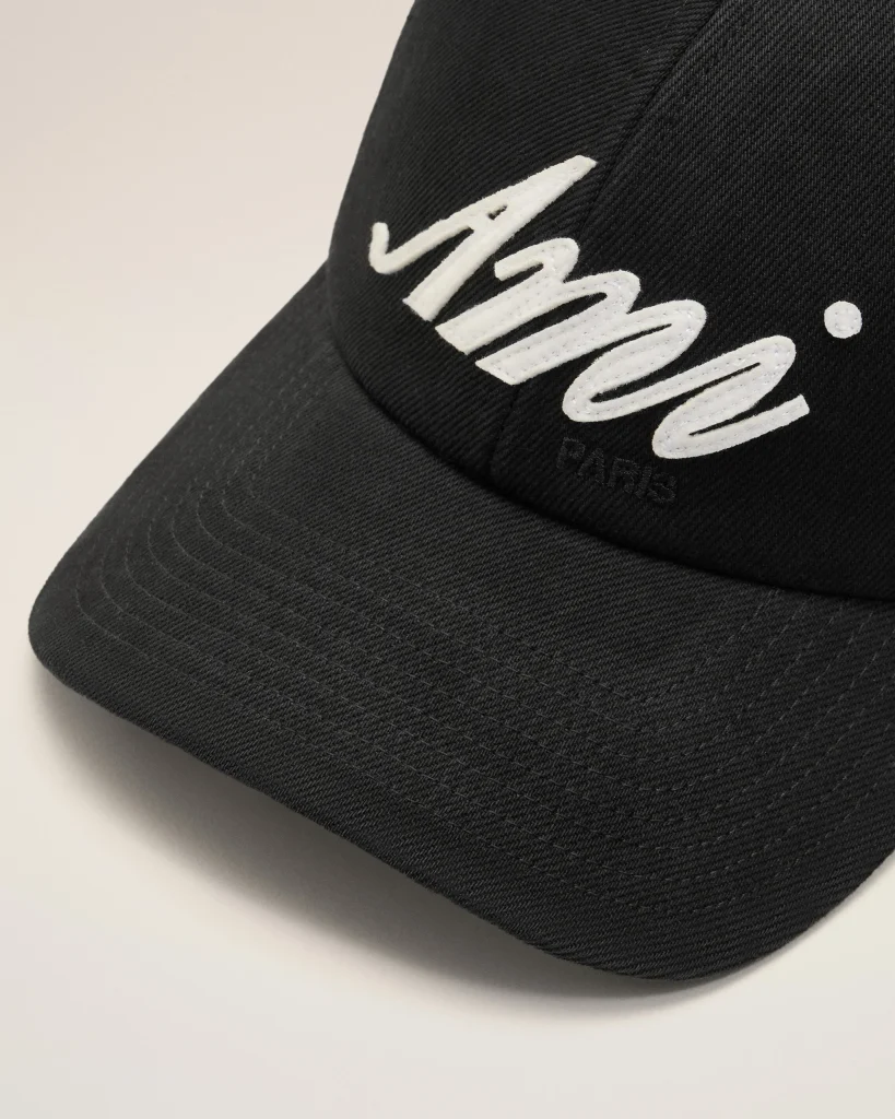 Close-up of a black cap with white embroidered cursive lettering on the front panel (partially visible).