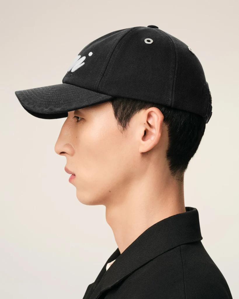 Side profile of a person wearing a black baseball cap against a light beige background.