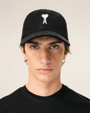 Close-up of a person wearing a black baseball cap with a white heart-shaped logo on the front.
