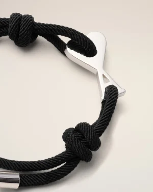 Close-up of a black twisted rope bracelet with a silver heart-shaped clasp against a pale background