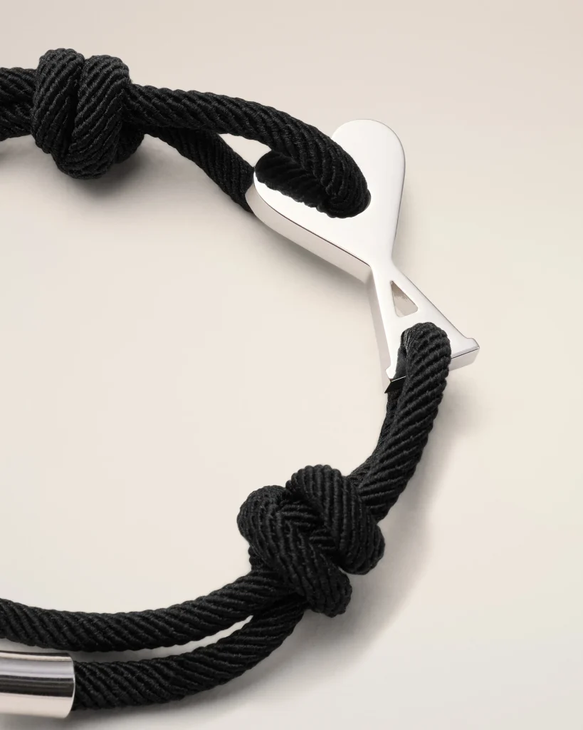 Close-up of a black twisted rope bracelet with a silver heart-shaped clasp against a pale background