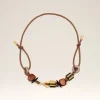 Brown leather necklace with gold clasps and multi-colored beads laid against a pale background, shown in a curved arc.