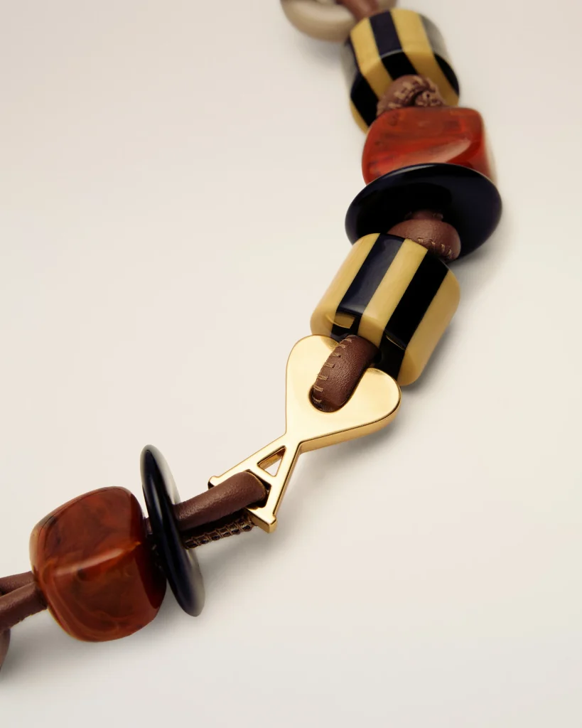 Close-up of a beaded bracelet with yellow and black striped beads, brown leather strands, and a gold heart-shaped clasp