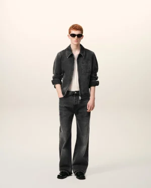 Red-haired model wearing a black denim jacket, white shirt, and dark jeans with sunglasses, facing the camera.
